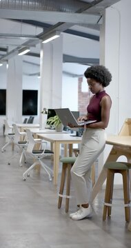 Vertical video: Adult woman in maroon top reading laptop leaning on table typing while at work