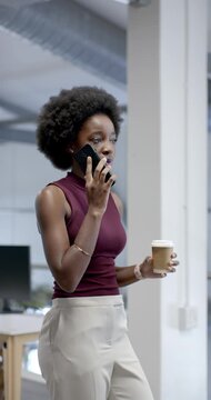 Vertical video: African American woman taking call holding cup moving cell to ear at work
