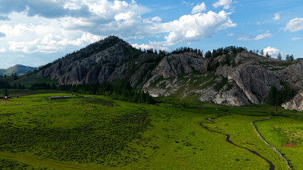 Breathtaking high-angle panoramic aerial view of an expansive green valley with dramatic rocky mountains and lush meadows on a sunny day. © OlTarakanov