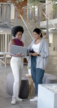 Vertical video: Diverse female coworkers angling laptop, pointing at phone and confirming in atrium