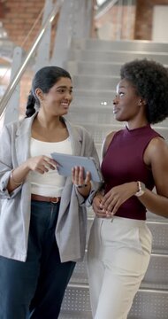 Vertical video: Indian, African women at work on stairs Indian pointing at tablet African tapping