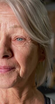 Vertical video: Senior woman with gray hair reacting to off-camera cue blinking and smiling at home