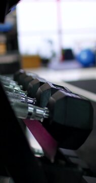 Vertical video: Camera is tilting, showcasing hex weights on rack with loop bands and window bokeh