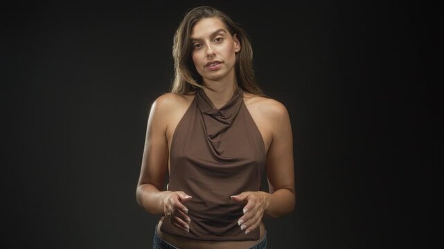 Woman with bare shoulders in brown halter top gesturing with hands and pursed lips in studio; thoughtful explanation.