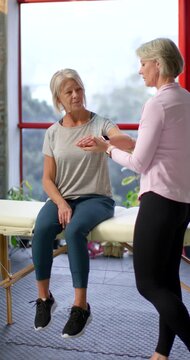 Vertical video: Senior client on table as female therapist reaching wrist guiding motion for rehab