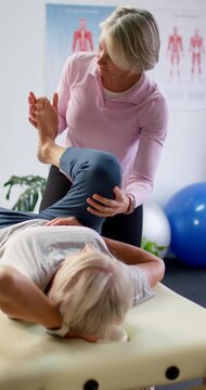 Vertical video: Female clinician assessing female patient, lifting leg, rotating knee on table