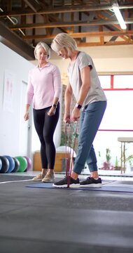 Vertical video: Female trainer guiding while client stepping on band, hinging in studio for posture