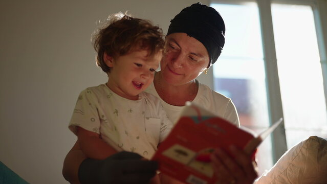 Mother and toddler son read a colorful picture book together on the living room sofa, sharing joyful learning, affection, imagination and meaningful family connection