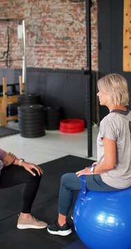 Vertical video: Female trainer and client reaching, guiding balance on blue ball while clapping