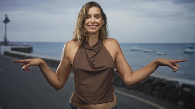 Woman pointing fingers outward with bare shoulders visible and brown halter top on street by ocean promenade pier; playful ambiguity.