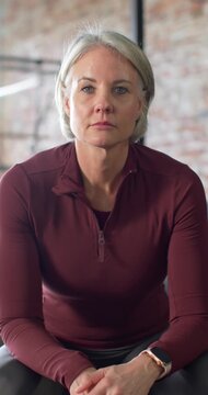 Vertical video: Senior woman in studio seeing left light, lifting head, meeting gaze, showing watch