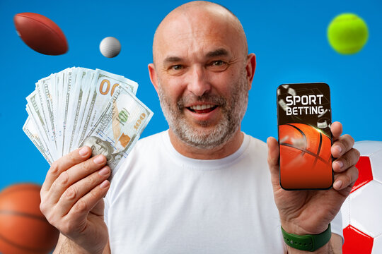 Man holding cash and phone while showing interest in sports betting with various sports equipment around