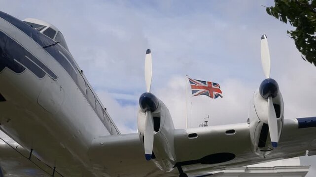 A vintage propeller airplane with a waving British flag behind it.