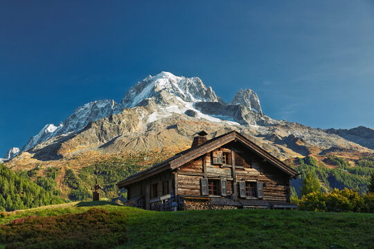 Traditional wooden chalet of Auberint La Boerne in front of snow-capped Aiguille Verte mountain on the Tour du Mont Blanc trail, France.