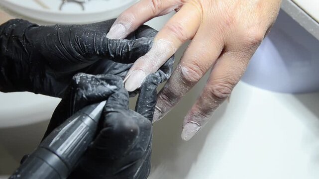 Professional manicurist removing cuticle with an electric nail drill during a hardware manicure. Close-up of nail preparation and cuticle care in a beauty salon.
