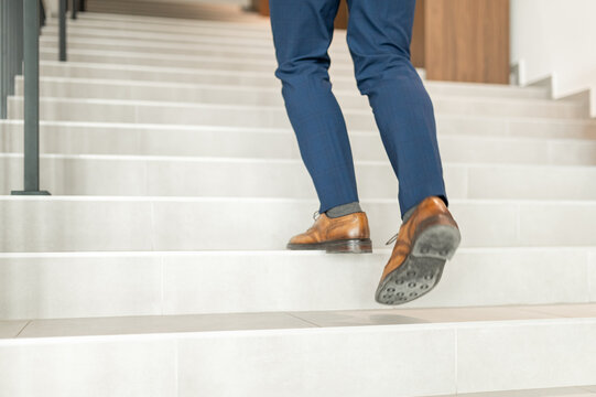 Business person's legs and feet climbing up modern stairs, representing professional growth, ambition, and upward movement in a corporate environment