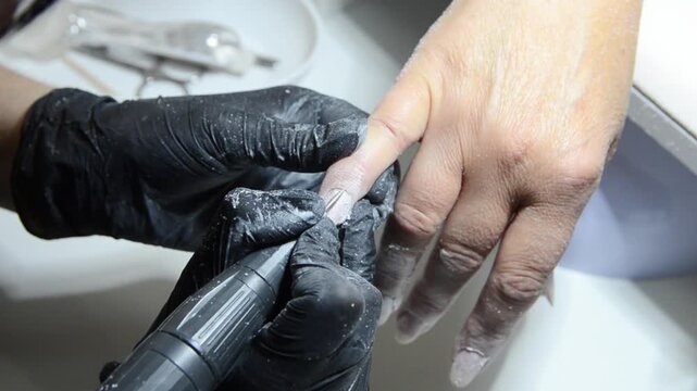 Professional manicurist removing cuticle with an electric nail drill during a hardware manicure. Close-up of nail preparation and cuticle care in a beauty salon.