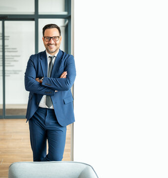 Business professional in blue suit smiling, standing with arms crossed, portraying confidence, success, and expertise in an office environment, ready for corporate challenges