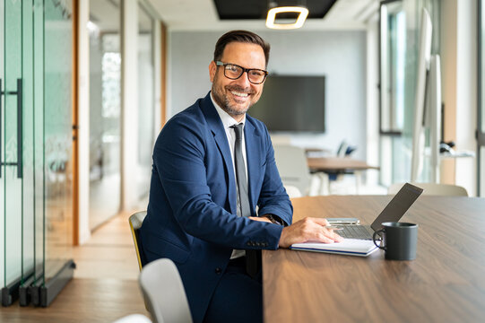 Business professional smiling and looking at camera. Working with a laptop and notebook at a conference table. Symbolizing corporate achievement. Leadership