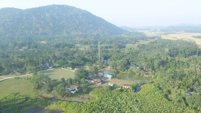 A high panorama reveals village homes, pond, greenery and distant hills, presenting the wider rural environment of Jalukbari, Assam.