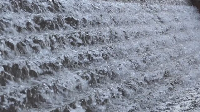Water cascading down textured stone steps of a waterfall feature.&nbsp;