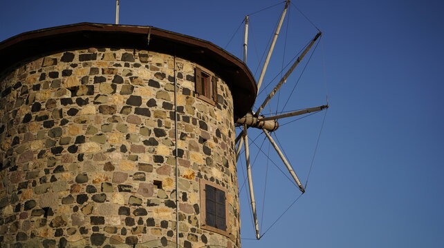 Close-up shot of historic stone windmill with wooden sails in Cunda Island Ayvalik against blue sky