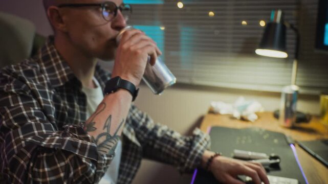 Caucasian young adult man typing on keyboard and drinking energy drink from can while gaming, handheld shot. Clip represents screen addiction and unhealthy tech habits