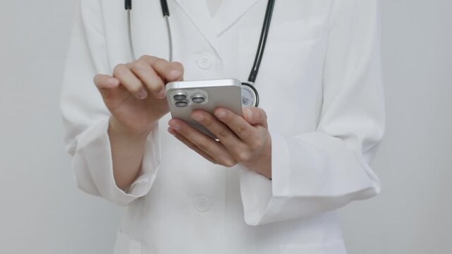 Close-up of female doctor hands using smartphone in front of white background