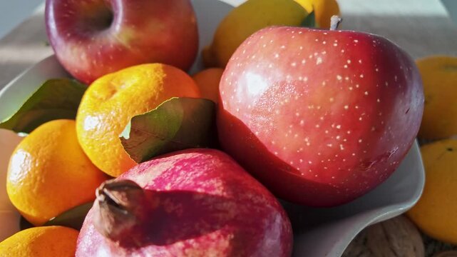 Closeup of assorted harvest fruits including mandarins red apples and pomegranate arranged together on plate.