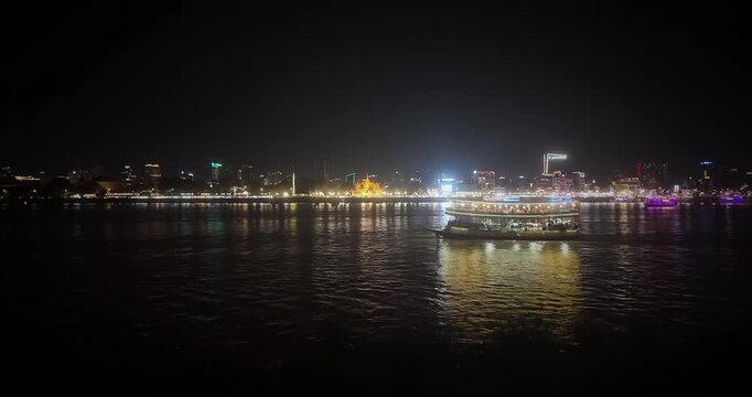 Night view of Phnom Penh skyline featuring the illuminated Royal Palace and a cruise boat crossing the Mekong River.