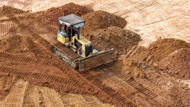 A bulldozer is moving dirt and grading the ground at a work site with piles of soil