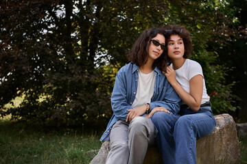 Fototapeta premium Love blooms in the green park as two young women share a tender moment