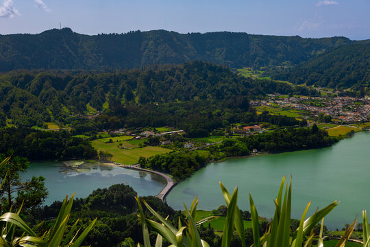 Lagoa das Sete Cidades showing the twin volcanic lakes, one blue and one green, separated by a bridge with the surrounding green hills, village, and lush vegetation. View from Cerrado das Freiras view