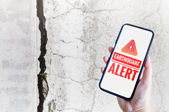 Earthquake alert on smartphone over crack wall background, emergency alert, Natural Disaster warning