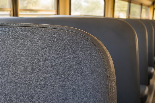 Back to school with empty bus seats, showing well-worn gray cushioning and soft textured fabric in sunlight.