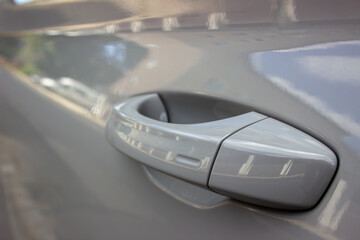 Fototapeta premium Close-up of a car door handle on a silver vehicle with a reflective, sunlit background.