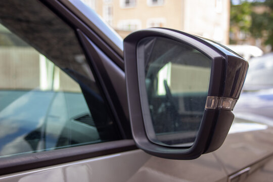 Close-up of a car side mirror reflecting a sunlit urban street with buildings and trees.