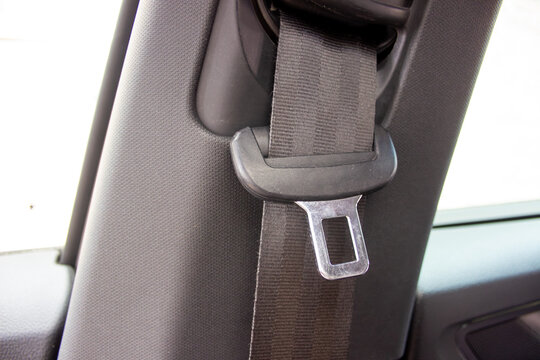 Close-up of a car seatbelt buckle and strap against dark fabric upholstery.