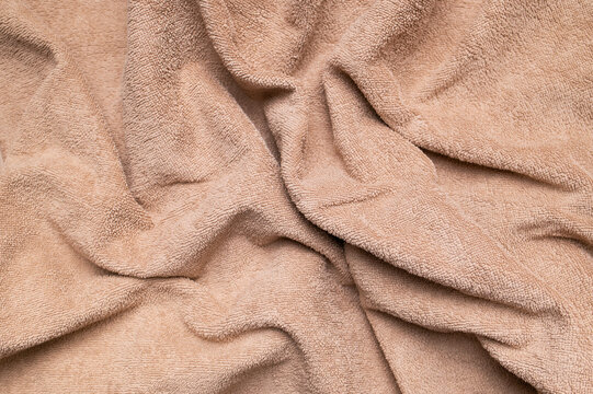 Folded brown terry towel fills frame in closeup, showing cotton texture, plush surface and soft fabric folds for bath styling, textile advertising, spa branding and home lifestyle imagery.