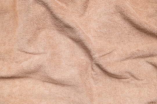 Close-up texture of terry cotton towel. Brown bath towel with folds top view. Abstract fabric background. Concept of soft fabric and natural textiles, spa, wellness, hotel services