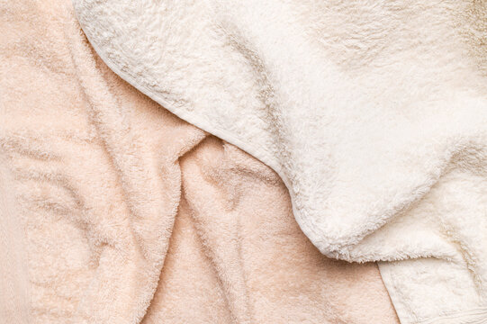 Abstract fabric background with folds. Close-up of terry cotton towel. Texture of soft, fuzzy light beige fabric, space for text, top view. Concept of softness, purity and bath textiles