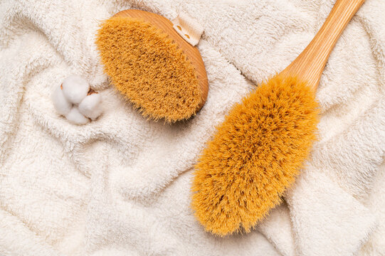 Massage brush with natural bristles on white cotton terry towel creates clean spa imagery for body care, wellness branding, home routines, personal grooming, and beauty product marketing.