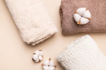 Rolled cotton towels and cotton flowers on beige surface present soft bath textile styling. Plush fabric, natural detail and neutral tones suit spa branding, hospitality visuals and home wellness. © olgaarkhipenko