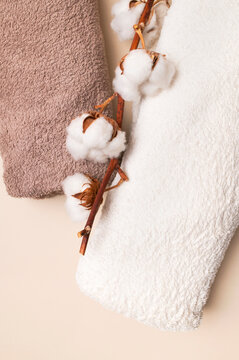 Folded terry bath towels in pastel shades and cotton branch on light beige background, top view. Natural cotton towels for spa, hygiene, body care. Eco-friendly fabric and home textile concept.