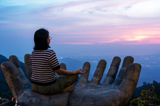 Woman sitting on a Buddha hand looking over sunset in Bukit Kokol Kota Kinabalu Sabah