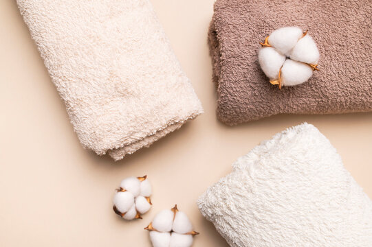 Rolled cotton towels and cotton flowers on beige surface present soft bath textile styling. Plush fabric, natural detail and neutral tones suit spa branding, hospitality visuals and home wellness.