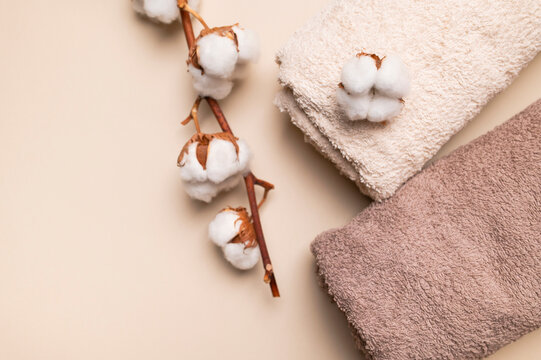 Folded cotton towels and white cotton flowers on beige background create calm spa styling. Soft textile, natural fibers and clean bath accessories support wellness, hotel and home care marketing.