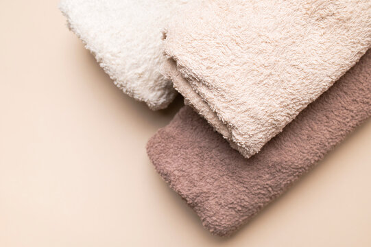 Folded terry towels in beige and brown tones create soft textile styling on beige background. Plush fabric, warm texture and neutral colors suit spa, hotel, bathroom and home care marketing.