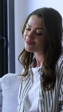 A relaxed young woman sits comfortably on a sofa, happily finishing her work or study on a laptop. She closes the device, stretches, and savors a moment of peace and satisfaction in her modern home.