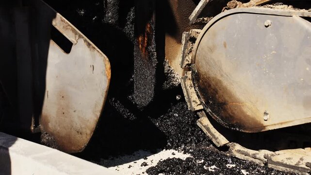 Hot asphalt mixture moving through paving machine during road construction